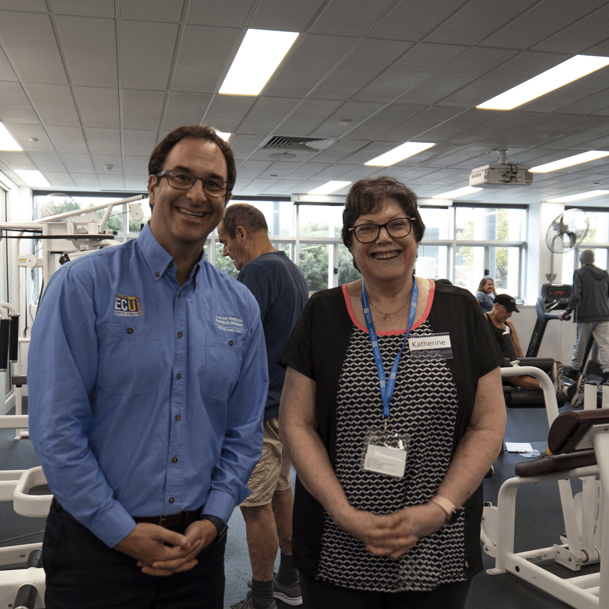 A man and a woman stand smiling at the camera in a gym