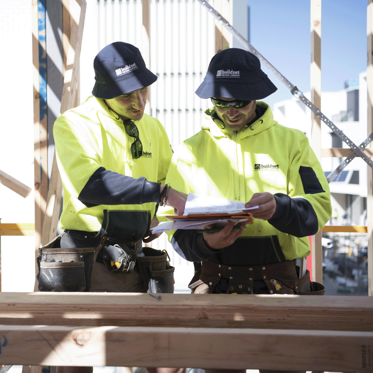 Two men on a job site look at some paper work whilst wearing sun protection